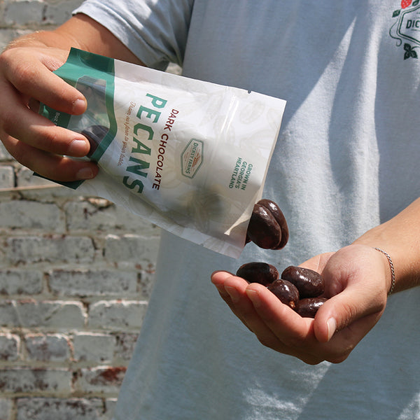 a person is holding a bag of dark chocolate pecans