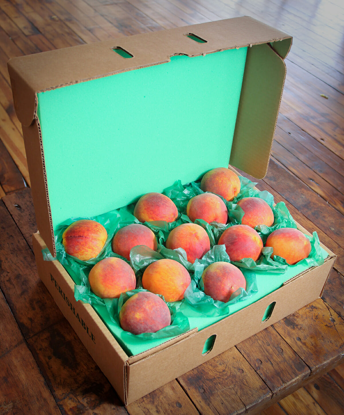 a cardboard box filled with peaches with green wrapping